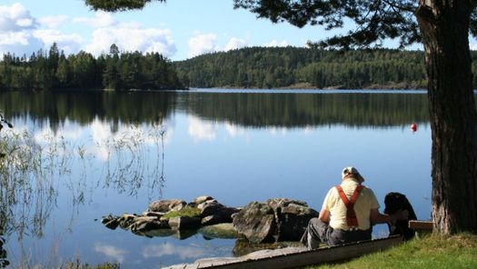 Mann sitter ved stille innsjø på en varm sommerdag med blå himmel