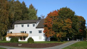 Fasaden på Fløvik Bo- og Omsorgshjem med stor tre ved siden av